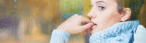 A person gazes pensively through a rain-covered window.