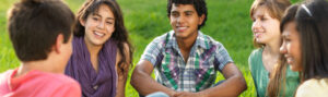 A smiling young man sitting outdoors on grass.